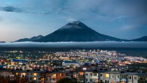 Photo of dusk over illuminated buildings of Petropavlovsk-Kamchatsky in front of volcano Koryaksky